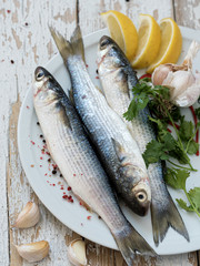 Fresh mullet is on a white plate. Sea fish. Spices, pepper, lemon. Located on a white wooden vintage background. View from above.