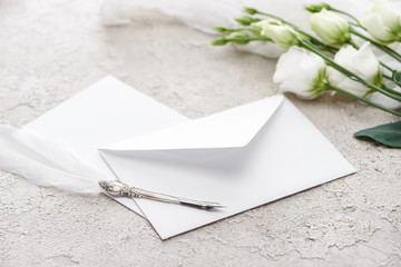 white envelope near eustoma flowers and quill pen on grey textured surface