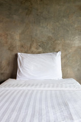 Pillows on comfortable bed with exposed concrete wall in modern bedroom.