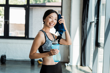 Fototapeta premium happy girl holding sport bottle while wiping sweat with blue towel