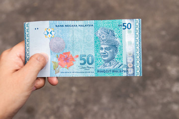 Fifty Ringgit Malaysia bank note on hand isolated on grey background.