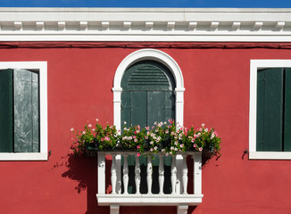 Fototapeta na wymiar Beautiful window with shutters and flowers on the one windowsill in one of the houses on the island of Burano. Venice, Italy