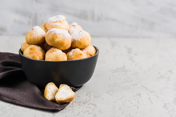 Eclairs with cottage cheese in a black bowl on a light background closeup with copyspace