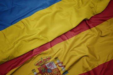 waving colorful flag of spain and national flag of ukraine.