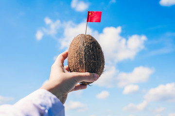 Tropical coconut with Chinese flag in the form of a toothpick in female hands. Travel concept.  Tourism in China