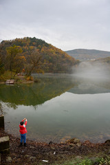 Young boy, kid in red coat fishing. Lake in the fog, surrounded by colorful forests. Wood in autumn. Child fishing. Lake in Europe, Slovenia, Koper, Vanganel. Vanganelsko jezero.