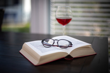 a pair of glasses lies on an open book and in the background is a wine glass