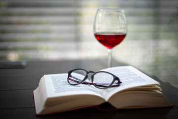 a pair of glasses lies on an open book and in the background is a wine glass