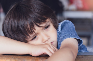 Upset little boy sitting alone on table, Kid sad face,Unhappy child laying his head on hand and...