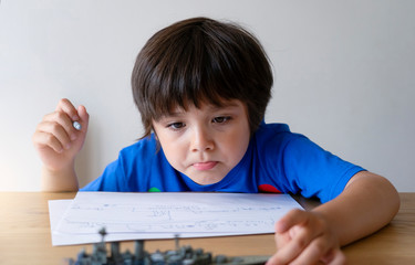 Portrait Cute little schoolboy drawing battleship, Child playing with model ship toy and sketching on paper, Indoors actvitiy concept