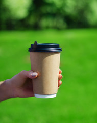 A Cup of coffee on a background of grass. A glass in a woman's hand.