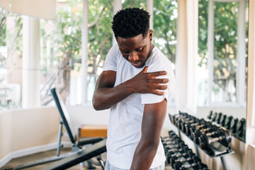 Side view of muscular African American man standing and suffering from shoulder pain during workout with dumbbells. Sportsman holding sore shoulder in gym - 283787886