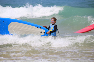Jeune enfant qui début le surf et porte sa planche