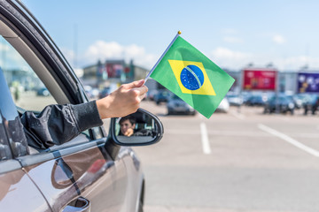 Boy holding Flag of Brazil from the open car window on the parking of the shopping mall. Concept
