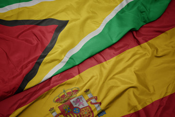 waving colorful flag of spain and national flag of guyana.