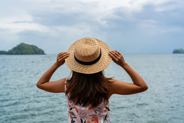 Beautiful young woman holding hat looking at the tropical beach.