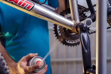 Closeup of male hands cleaning and oiling a bicycle chain and gear with oil spray. Working process