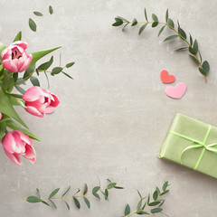 Springtime flat lay with bunch of pink tulips, eucalyptus leaves and gift boxes on stone