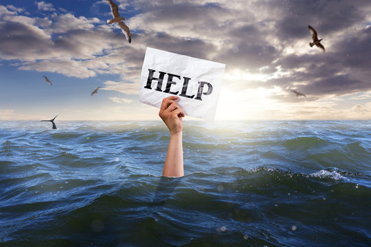 single hand of drowning man holding white paper with the word HELP