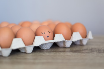 Egg with unhappy, sad angry face in the basket with other eggs.