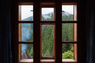Wooden window behind which a mountain forest is visible.