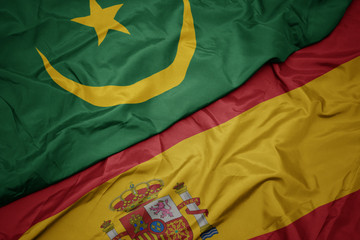 waving colorful flag of spain and national flag of mauritania.