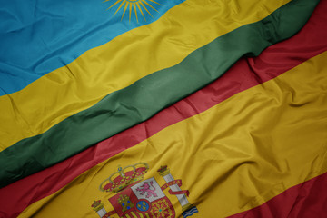 waving colorful flag of spain and national flag of rwanda.