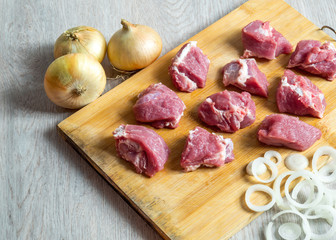 Pieces of raw beef and onion on cutting board