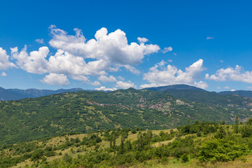 Typical greek summer landscape. Small village on the green hillside with clouds on blue sky. Greece.