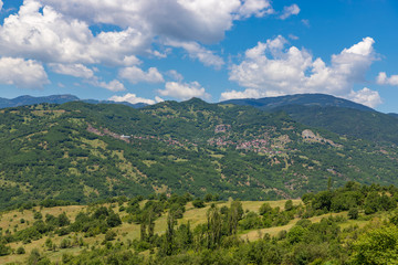 Fototapeta na wymiar Typical greek summer landscape. Small village on the green hillside with clouds on blue sky. Greece.