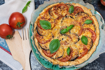 Homemade tasty kish pie with basil, cheese, tomatoes and eggplants on dark table top view.