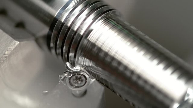 SLOW MOTION, MACRO, DOF: Sharp blade cuts a groove into the side of a metal workpiece as it is being processed into a bolt by lathing equipment. Twisted chips break off a small rod during threading