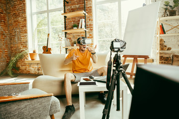 Full of emotions. Caucasian male blogger with professional camera recording video review of VR glasses at home. Blogging, videoblog, vlogging. Man using virtual reality headset while streaming live.