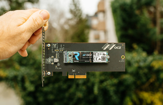 PARIS, FRANCE - NOV 28, 2017: Man hand holding NVME PCIE SSD hard drive disk with itsh adapter to the PCIE slot made by Toshiba OCZ RD400 with high read and write speed