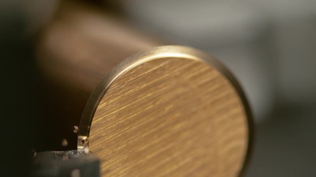 SLOW MOTION, MACRO, DOF: CNC blade shaves the edge of a golden cylinder, creating twisted shavings in the automated process. Lathing equipment cutting the outer layer of a shiny brass workpiece.
