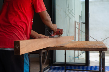 Closeup hand of carpenter holds electrical tool scrubbing the surface of wood