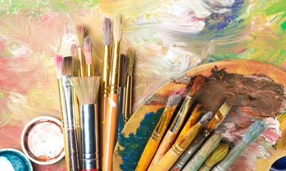 Artist paint brushes and paint cans of paint over bright watercolor background