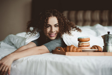 Happy woman wake up in hotel room with tasty breakfast lying in bed close up. Looking at camera....