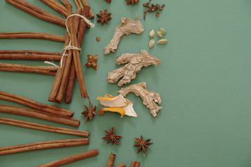 Cinnamon sticks and anise, cardamom, cloves, ginger, orange peel laid out on a green background. Spices for drinks and food. Mulled wine. Christmas still life. Flat light. Top view. With copy space.