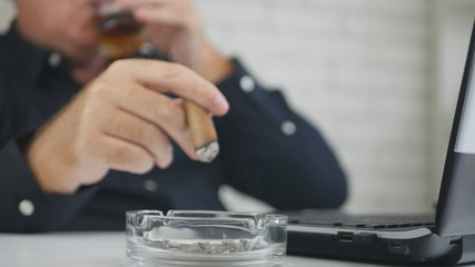 Fototapeta na wymiar Businessman Blurred Image Drinking Whisky Smoking Cigar and Working on Laptop