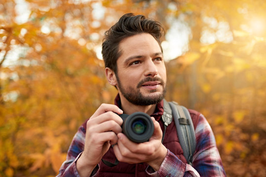 Attractive caucasian man taking pictures with a mirrorless camera through the forest in the fall in Canada