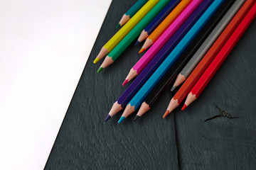 Colorful pencils and empty blank on a dark wooden table.