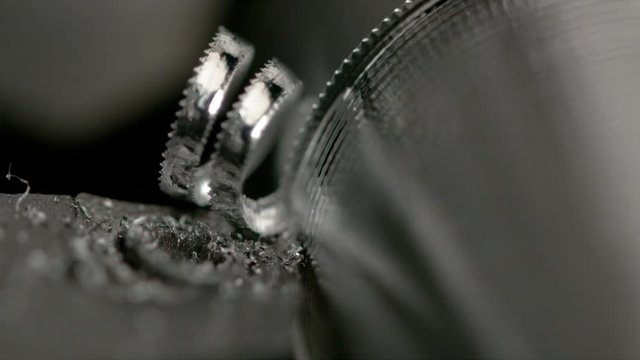 SLOW MOTION, MACRO, DOF: Long spirals of excess metal are created as the lathe tool carves grooves into a workpiece and creates a screw. Blade cuts into steel cylinder as it is processed into a bolt.