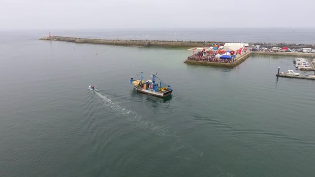 Aerial, pan drone shot, of a little motorboat, passing a fishing boat, at the port of Penice, on the coast of the city, on a cloudy, summer day, in Portugal