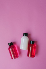 Group of small travel bottles for body care: shower gel, shampoo, balm, lotion on pink background. The composition of the flat layer of cosmetics Copy space.