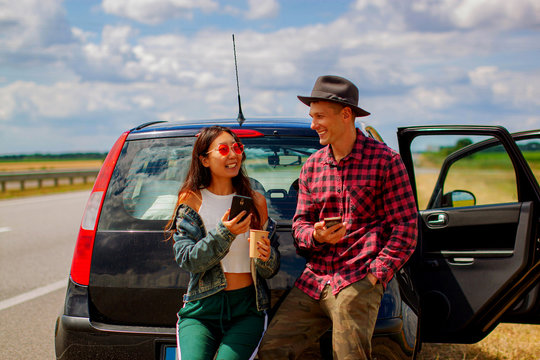 Young Attractive Couple Looking At Smart Phone Near A Car In The Trip.