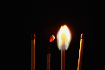 Four wooden matches on a black background. One is burnt, one is still burning and the other two are unlit.