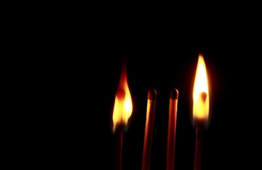 Four wooden matches on a black background. Two burning, two unlit.