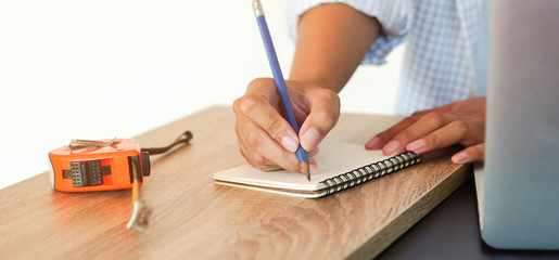close up on engineer woman using pencil for sketch design on page notebook with measuring at home office for repairing or renovate the old home concept