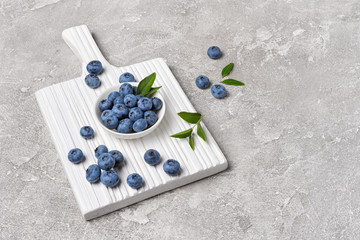 Fresh blueberry berries in white bowl on wooden board